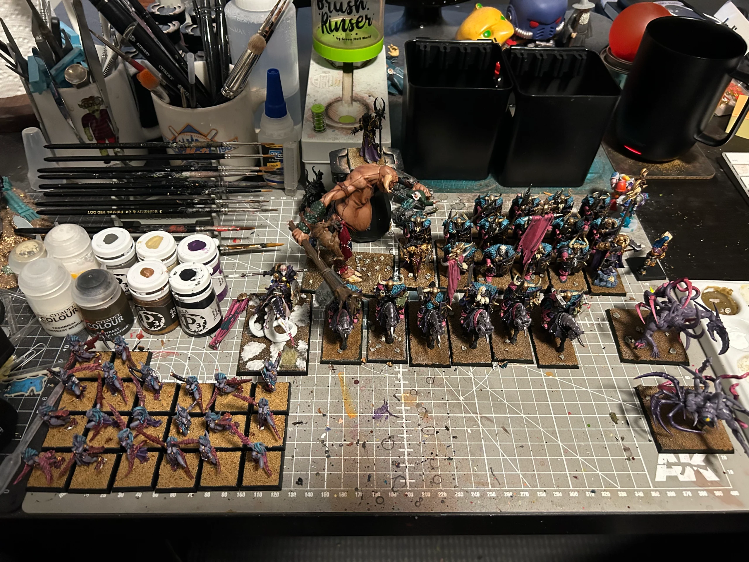 Photo of my paint desk littered with fully-painted Chaos Warrior models for Warhammer the Old World. The bases are a work-in-progress as I update them to the new sizes.