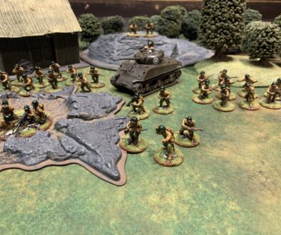 Photo of an approximately 650 point force of American Bolt Action miniatures with a farmhouse, forest, rock, and crater I the background.