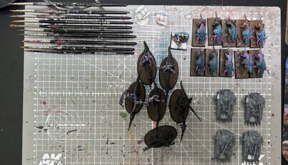 Top-down photo of my cleaned-up paint table featuring only a rack of brushes and three projects: some Slaanesh cavalry, some war hounds of chaos, and a quartet of Kratos tanks for Legions Imperialis.