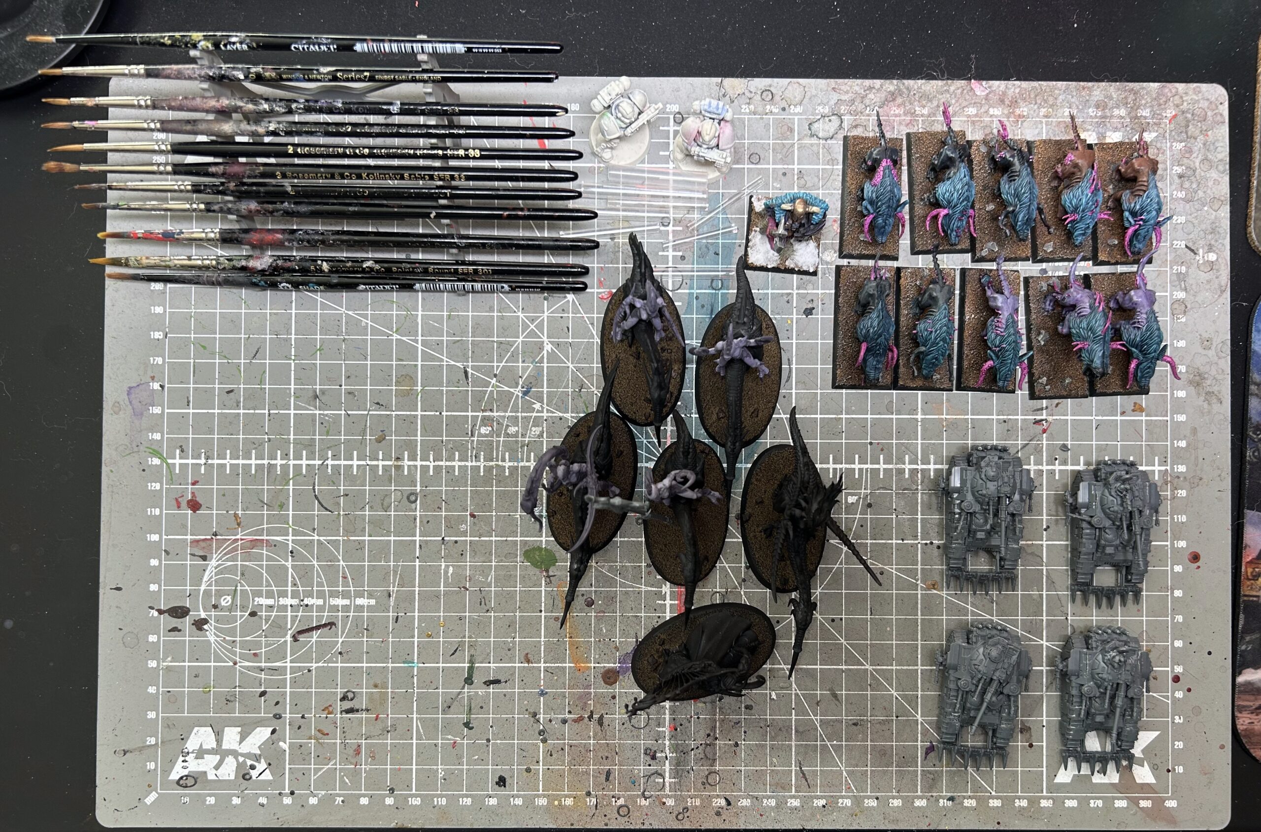 Top-down photo of my cleaned-up paint table featuring only a rack of brushes and three projects: some Slaanesh cavalry, some war hounds of chaos, and a quartet of Kratos tanks for Legions Imperialis.